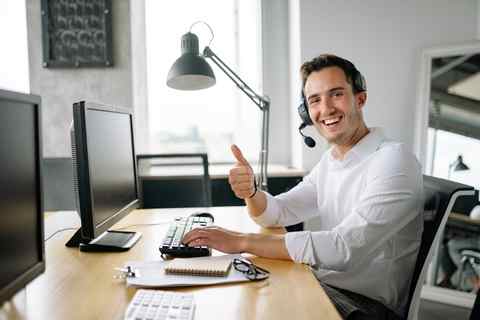 Kundenservice im Büro Mann im Callcenter mit Headset, lächelnd und Daumen hoch.