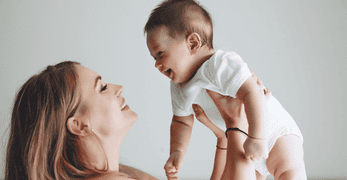 aktionsseite_babybonus_347x180 Eine junge Frau hält ein Baby hoch